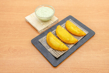 Colombian yellow corn flour empanadas stuffed with chicken stew with peppers on top of a black slate plate and a bowl of dip sauce