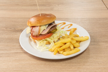 Classic beef burger with bacon, ham, pickled cucumbers, tomato and onion and a side of French fries