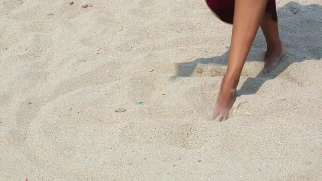 Female feet on the sand in a developing red dress. An african woman on the beach stands barefoot on a summer day. Enjoying nature.