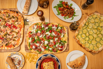 Set of Italian food dishes with olive oil, dehydrated tomato, zucchini pizza, pizza with burrata and serrano ham, pasta and calzone