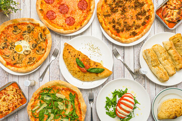 Typical Italian dishes on a restaurant table. Calzone, pizzas, capresse salad, meat lasagna and lots of arugula and basil