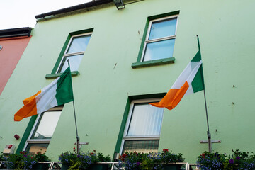 Two Irish flags mounted on a light green wall of a building in a town street