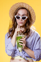 Girl in summer outfit wearing white trendy sunglasses and enjoying while drinking a Mojito cocktail. Posing on the yellow background