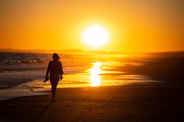 Fototapeta na wymiar Silueta de mujer caminando al ocaso en la playa en vacaciones