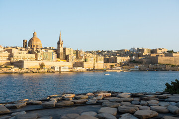 Landscape of Valetta skyline in Malta with boat passing. The stunning skyline of old Valletta, its churches and towers, its historic remparts from the Northern Harbour on golden hour.