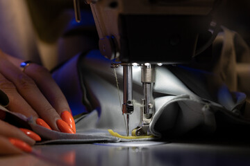 Closeup of seamstress sew clothes on sewing machine. Work with light of hardware lamp. Female hand hold steel needle with bobbin and presser foot on cloth material. Sewing industry production concept