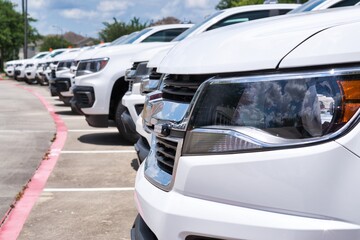 White generic vehicle fleet SUVs transportation parked row closeup front vehicle focus on foreground logistics industry.