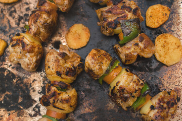 Flat lay view of grilling chicken skewers and potato slices on an electric backyard grill.