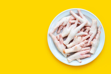 Raw chicken feet in white plate on yellow background.