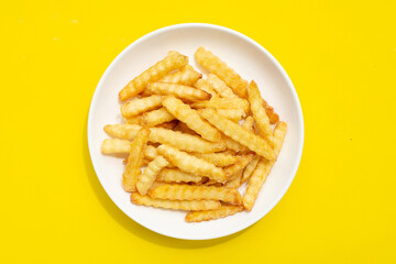 French fries in white plate on yellow background.