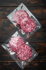 Burger beef veal cutlets in vacuum plastic, on old dark  wooden table background, top view flat lay