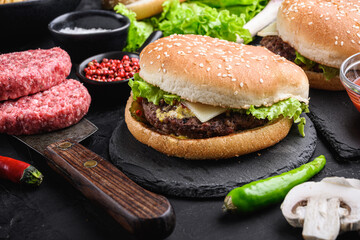 Craft beef burger in front of ingredients on black background