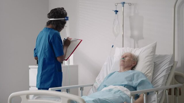 A black woman cardiologist doctor is talking to an old man patient lying on a hospital bed discussing rehabilitation after recovery. an infectious disease neurologist discusses a treatment strategy