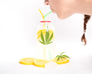 Girl drinking a cooling lemon cocktail with marijuana from a straw on white background