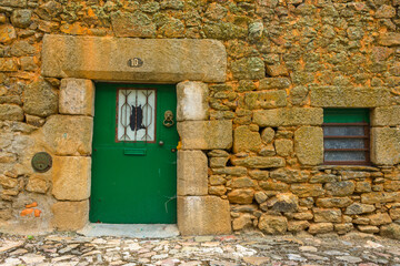 Green door with a black cat on the window in a stone house. Located on the portuguese ancient...