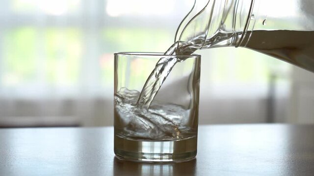Closeup male hands pouring water into glass from jug at kitchen background. 4k stock footage.