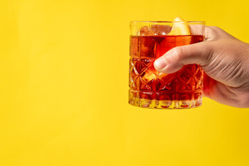 Close up view of negroni drink being hand held with yellow background.