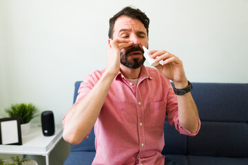 Latin man with a cold using a nasal spray - obrazy, fototapety, plakaty