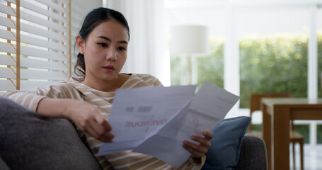 Upset tired young asia sad lady people sit sofa couch at home think hard worry in tax expense...