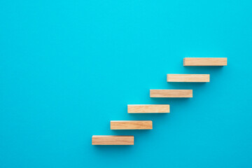 Flat lay of wooden blocks in shape of staircase step on blue background with copy space. Growth or...