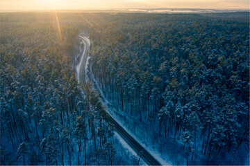Aerial view of a winter road with in the middle of a snowy forest at sunset