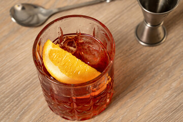 Close-up view of negroni cocktail on wooden surface with mixing spoon and jigger in the background