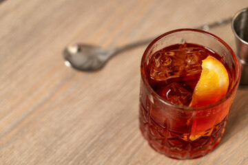 A swooping view of negroni cocktail with orange wedge on wooden surface with mixing spoon
