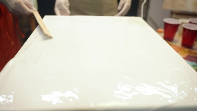 Women artists smering white glue on the canvas. Artistic collaboration in workshop.