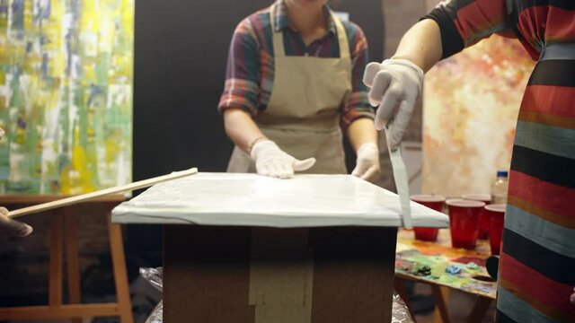 Women artists smering white glue on the canvas. Artistic collaboration in workshop.
