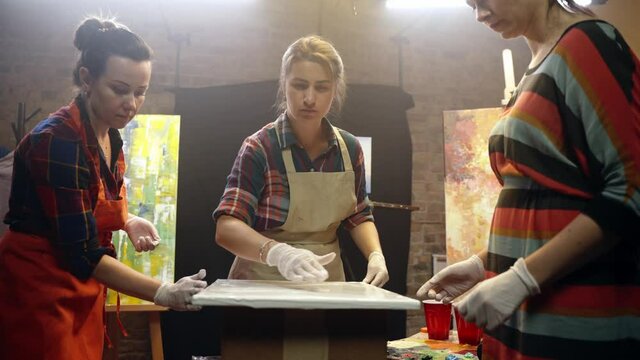 Women artists smering white glue on the canvas. Artistic collaboration in workshop.