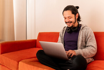 Young man doing home office sitting on a couch sofa at home in the living room