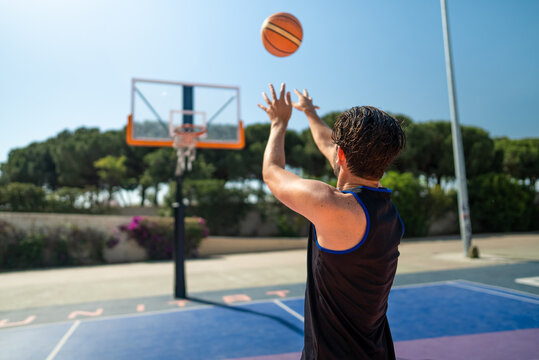 Male sportsman playing basketball throwing the ball at playground, back view. Precision shot
