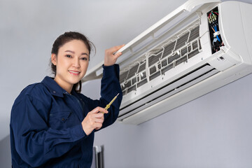 female electrician with screwdriver repairing air conditioner indoors