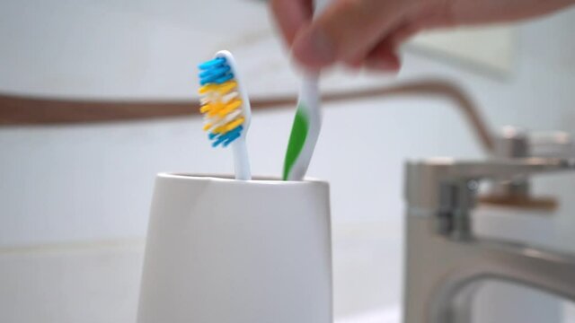 Picture of adult's hand which taking one toothbrush from plastic glass which standing near washbasin. 4k stock footage.