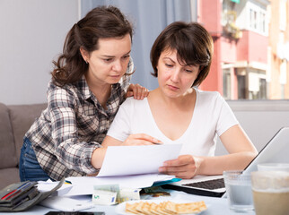 Fototapeta premium Portrait of serious women working with documents and using laptop at kitchen table