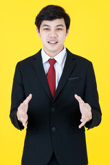 Vertical portrait shot of young Asian man in a black long sleeve suit with hand in pocket posing presenting and showing the empty space with the fingers isolated with yellow background in studio.