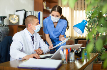 Obraz premium Head in protective mask gives task to assistant at office at table