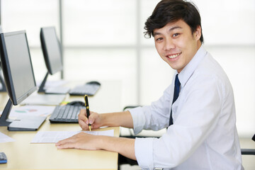 Portrait of a young adult professional businessman working on a paper document in front of a computer at the office table. Business manager signing the signature on the paperwork for approval