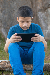 Fototapeta premium Latino boy playing with mobile sitting under the tree