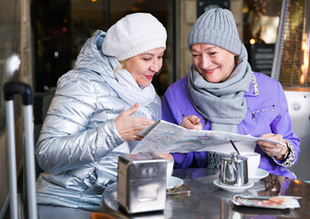 Happy mature ladies travellers relaxing at cozy outdoor cafe and looking map