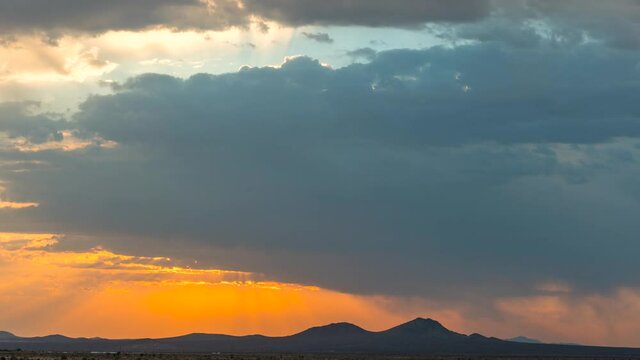 Colorful and dynamic cloudscape with a cloudburst over a mountain range in silhouette at sunrise - static time lapse