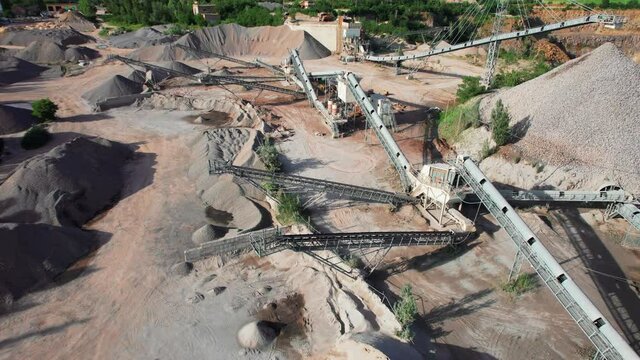 Arial view of the sand making plant in open-pit mining. Drone flies over excavators and tractor loading crushed stone and rock into dump truck. 4k stock footage.