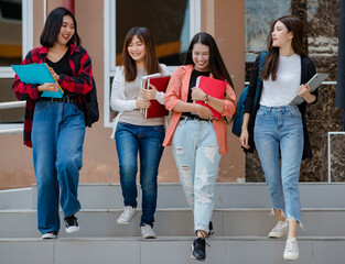 Fototapeta premium Group of four young attractive asian girls college students walking together down the stairs in university campus talking and laughing with joy. Concept for education and college students life