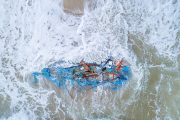 Broken boat and fishing nets washed up on a beach fish shape water sand debris waste plastic wood...