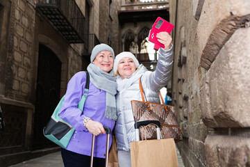 Happy elderly women tourists making selfie with phone during walk around city