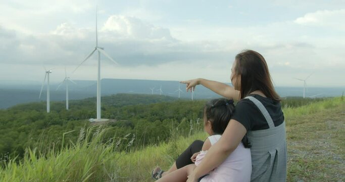Asian child girl and mother enjoy with beautiful scenery view of nature at the wind turbine field with fun together in slow motion shot.