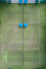 Tennis courts birds eye view top down drone aerial ariel UAV green grass blue umbrellas symmetrical no people copy space