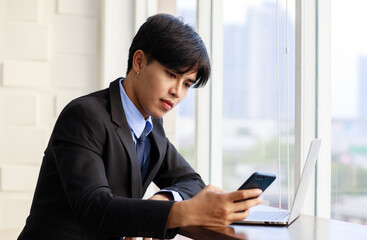 Fototapeta premium Portrait one young asian businessman are smart and handsome wearing black suit sitting chair talking phone while feel confident with smiling as smile on face looking at camera with laptop