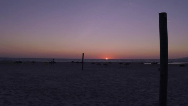 Suns hides in a tropical beach with palm trees umbrellas. Fast motion.