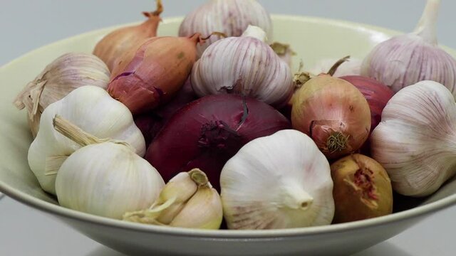 Spinning closeup of onions, garlic and shallots in white bowl